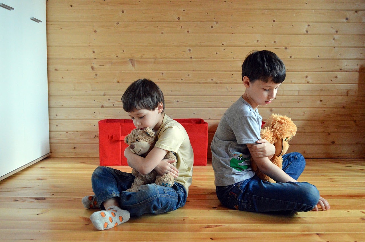 Immagine di 2 bambini seduti per terra che si danno le spalle e fanno il muso